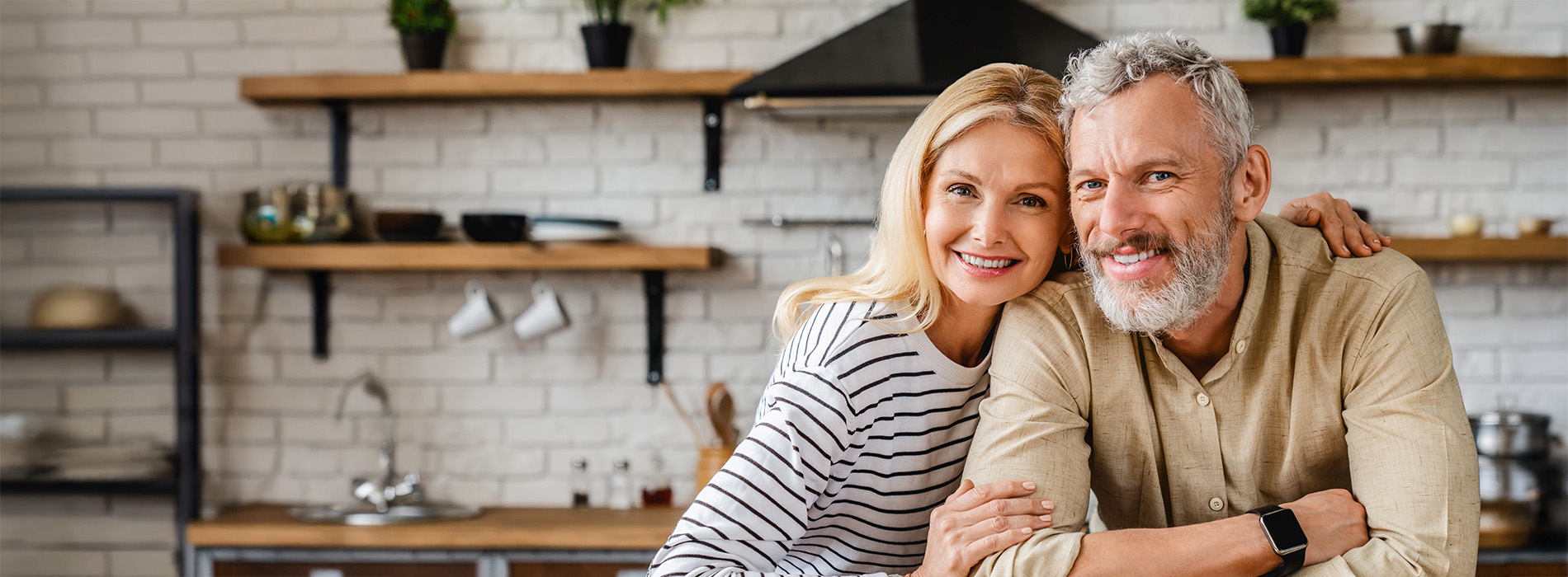 A man and woman posing together in a kitchen with a warm ambiance, smiling at the camera.