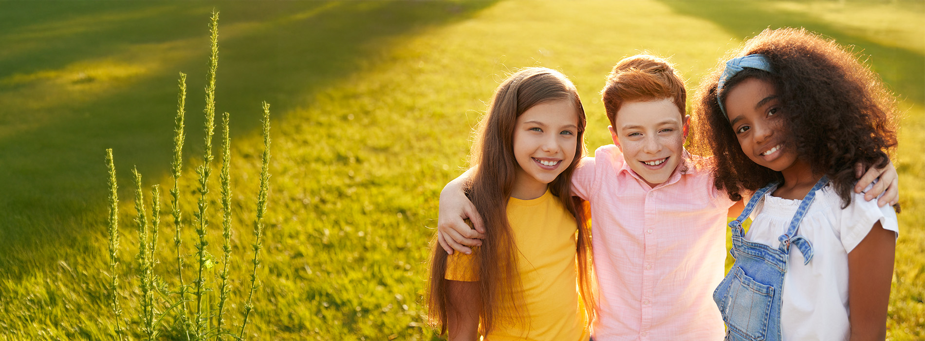The image shows three young individuals posing together outdoors during daylight  they are smiling and appear to be enjoying themselves.