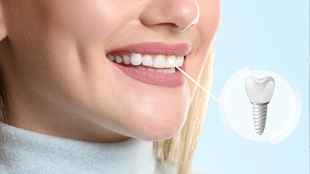 A woman smiling with a toothbrush in her mouth, showcasing an electric toothbrush with a visible plug inserted into its handle.