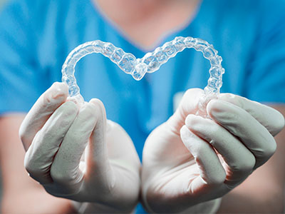 A dental hygienist wearing gloves holds up a heart-shaped dental retainer against their chest.