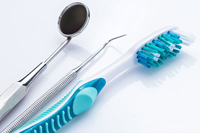 The image shows dental instruments including a pair of tweezers, a toothbrush with blue bristles, and other dental tools on a light background.