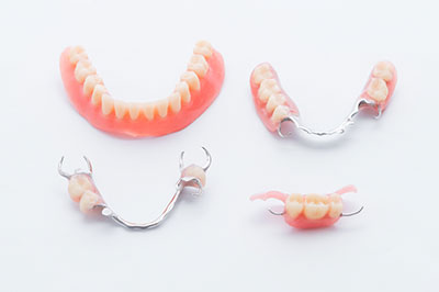 The image shows three pairs of dentures with pink gums, displayed on a white background.