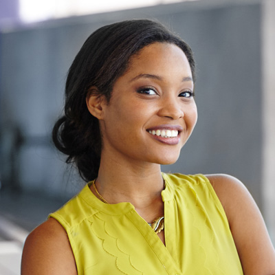 A young woman with a warm smile poses confidently against a backdrop of a building s wall.