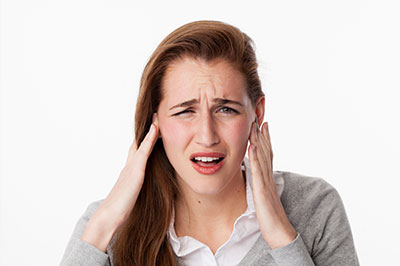 The image shows a woman with her hand on her head, appearing to be experiencing discomfort or pain, possibly related to an ear issue.