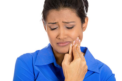 The image shows a woman with a concerned expression, holding her face with one hand while looking at something with the other, possibly related to dental care or health concerns.