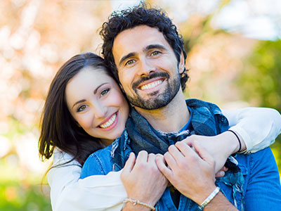 A couple embracing each other outdoors with a smile.