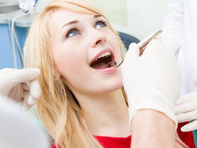 A woman receiving dental treatment with her mouth wide open while a dentist works on her teeth.