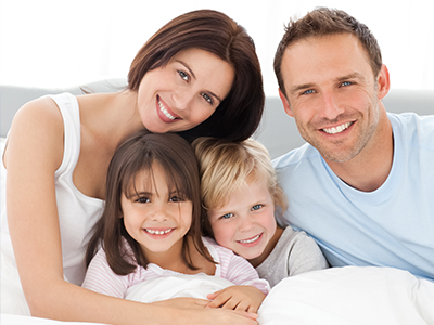 A family of five posing together on a bed with a white comforter.