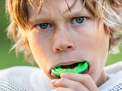 A young man with blonde hair and a serious expression, looking directly at the camera, holds a green object close to his mouth.